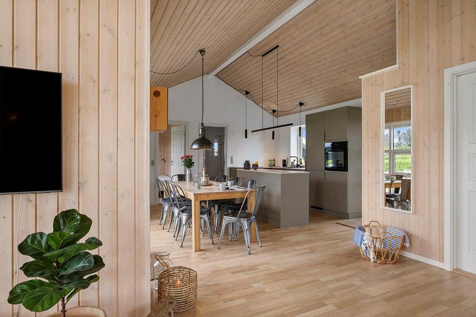 Ein Essbereich mit Holztisch und Metallstühlen. Küche mit Arbeitsplatte und Einbauküche. Holzwände und Boden.