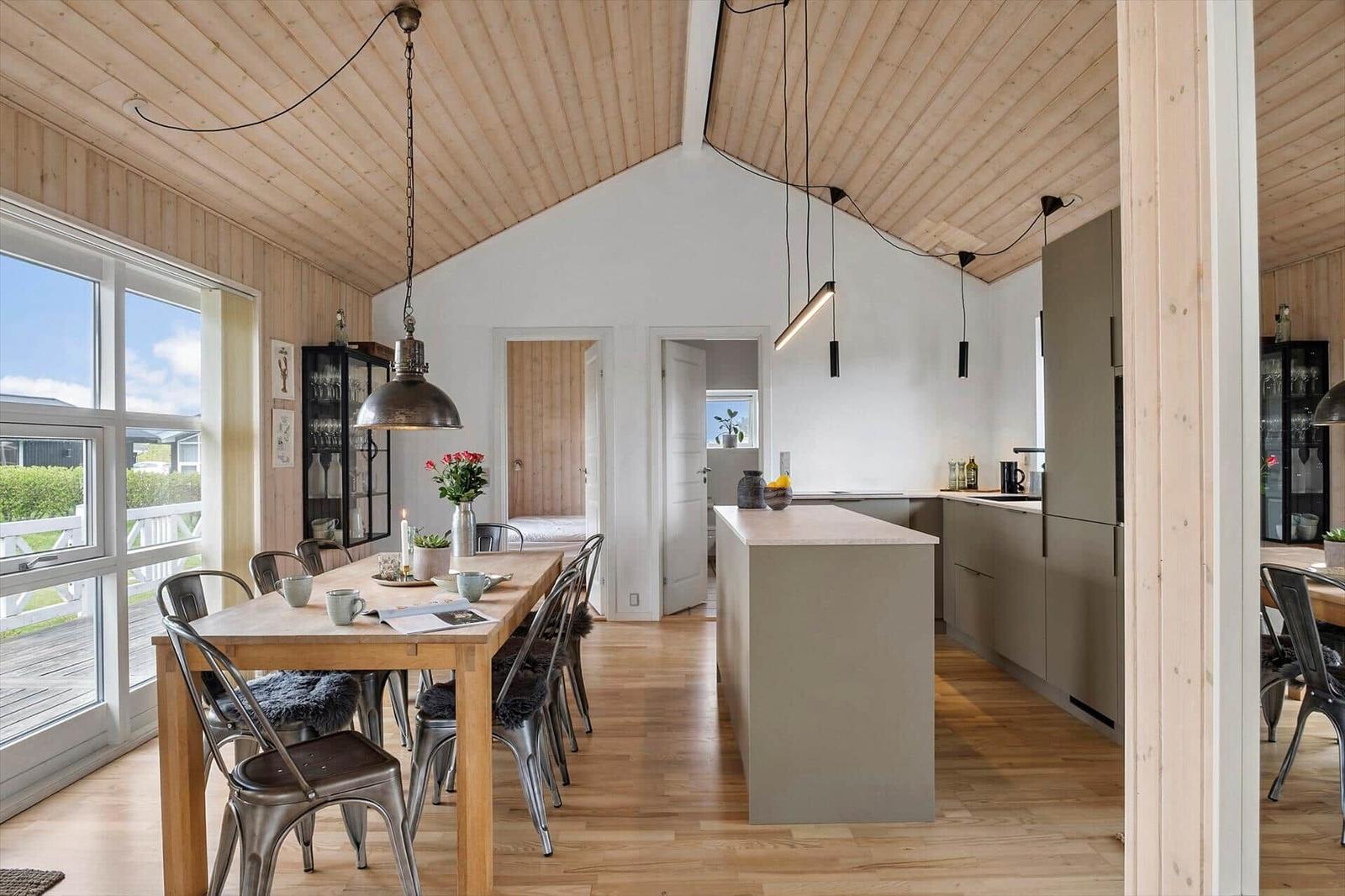 Essbereich mit Holztisch und Metallstühlen. Küche mit Kücheninsel und Holzdecke.