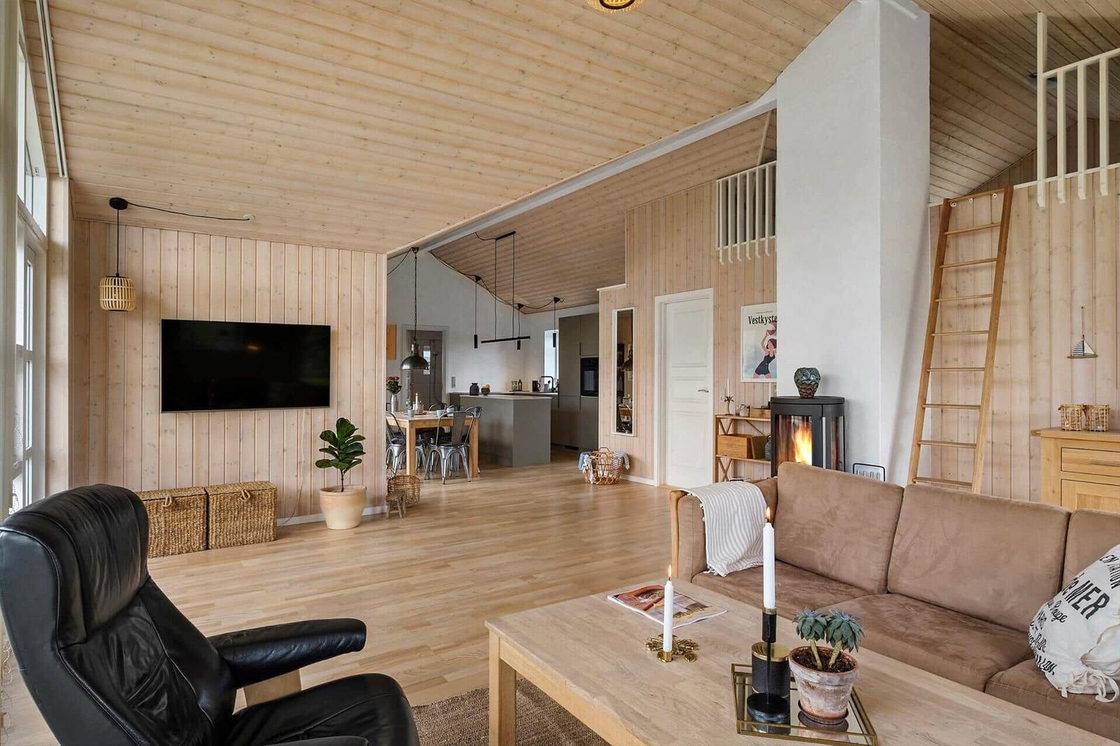 Wohnbereich mit Sofa, Fernseher und Kamin. Holzdecke und -wände. Treppe zur oberen Etage.
