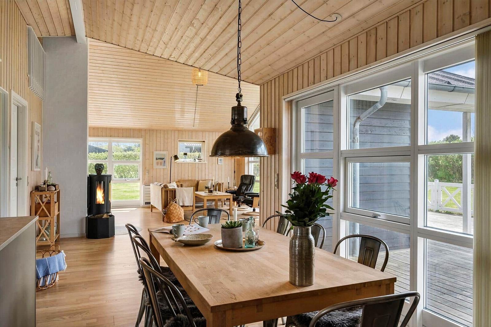 Essbereich mit Holztisch, Stühlen und Blumen. Durchgang in Wohnzimmer mit Kamin und Fenstern.