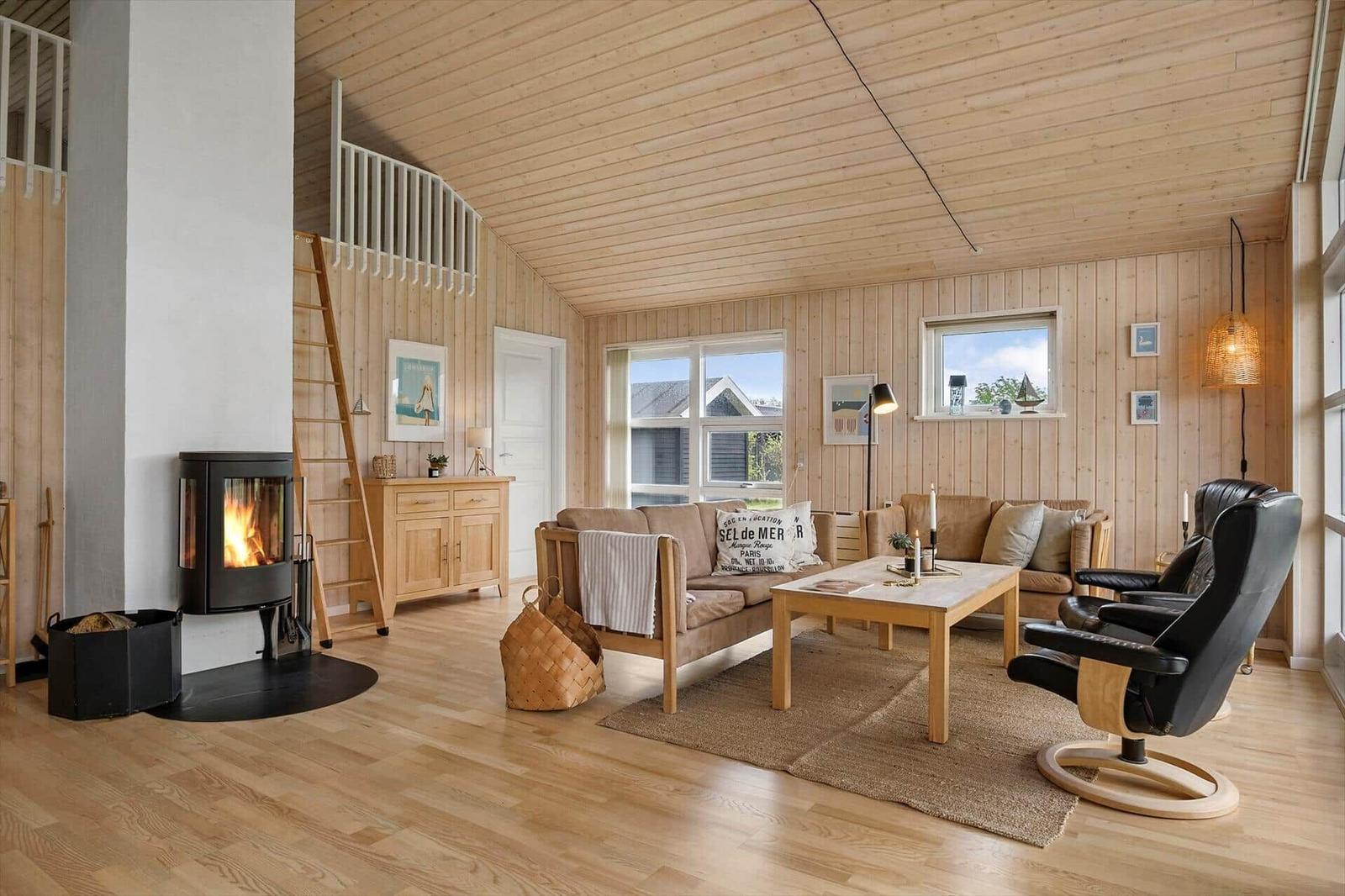 Wohnzimmer mit Holzdecke, Kamin und Sofa. Treppe zur oberen Etage.