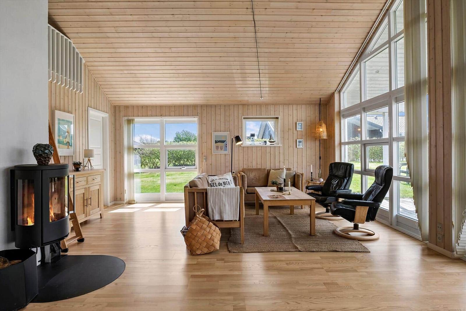Wohnzimmer mit Holzdecke, Kamin und großem Fenster. Möbel aus Holz und Leder.