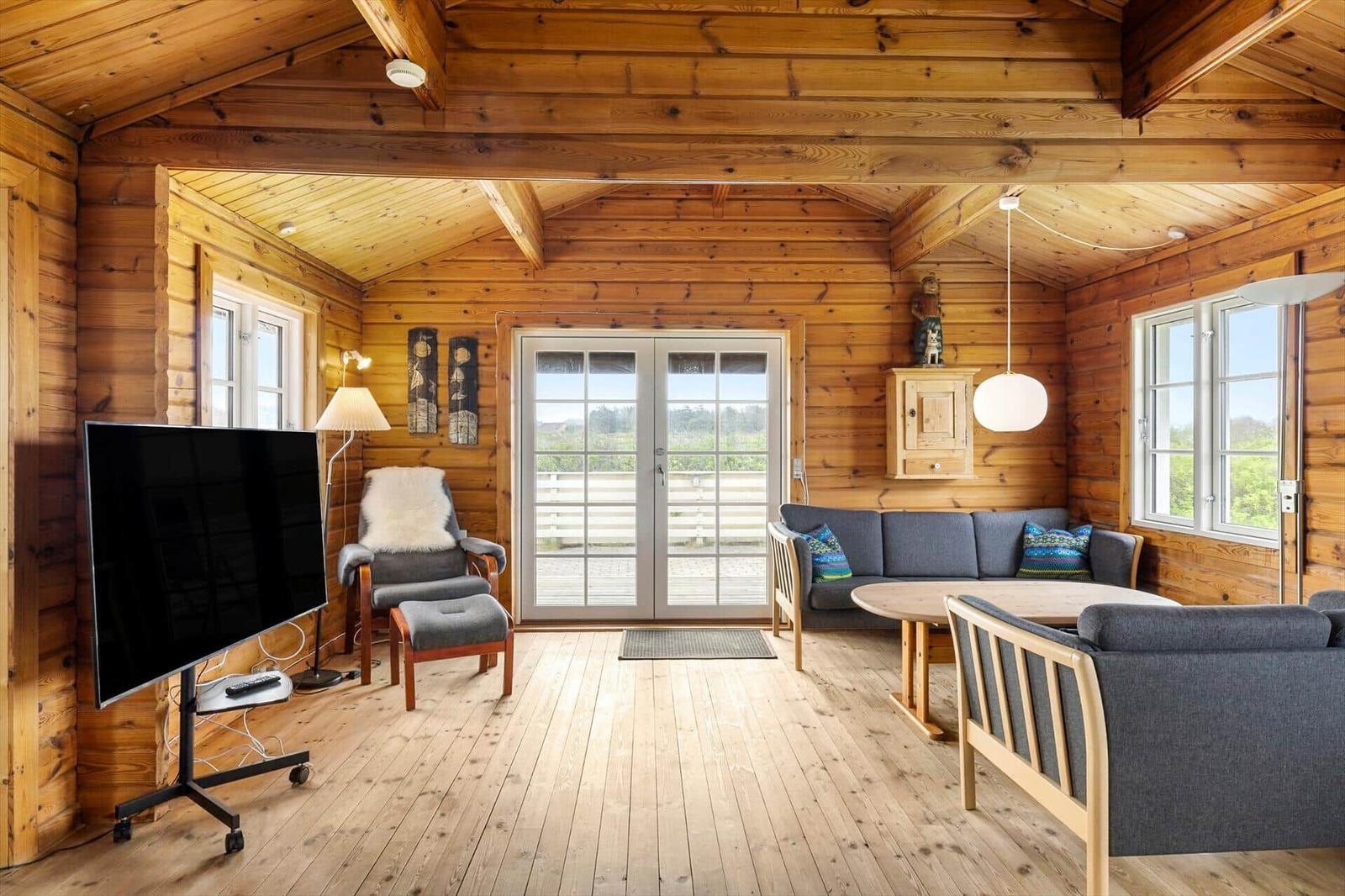 Wohnzimmer mit Holzwand, Sofa, Fernseher und Fenster zur Terrasse.