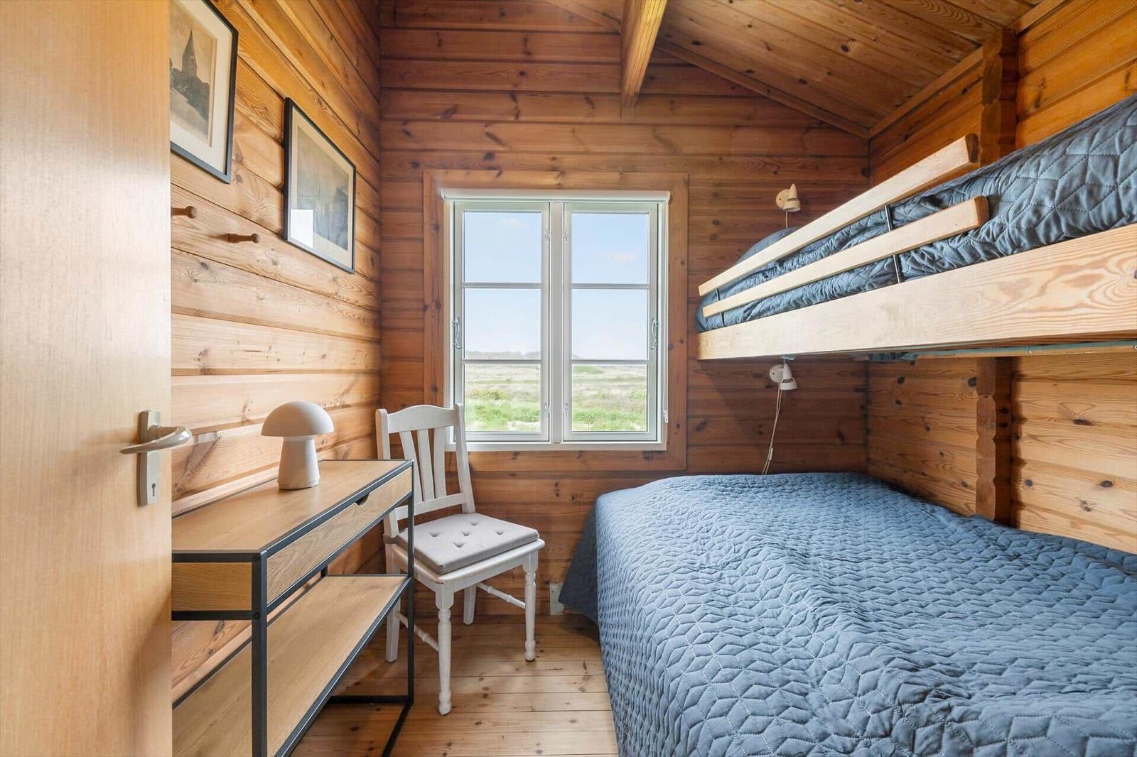 Ein Schlafzimmer mit Doppelbett, einem Fenster und einem Schreibtisch mit Stuhl.