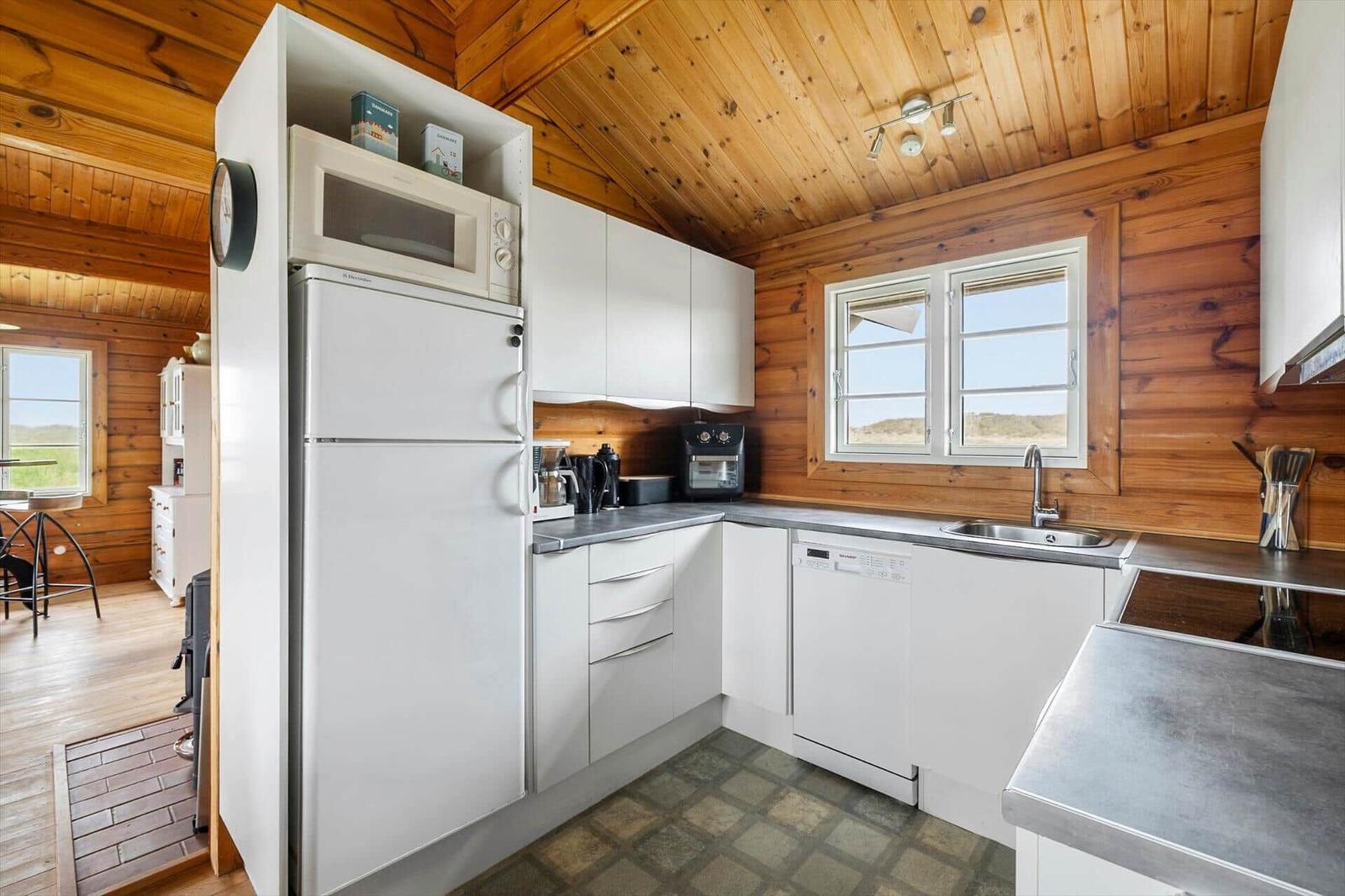 Küche mit weißen Schränken, Kühlschrank, Spüle und Fenster mit Blick auf Landschaft.