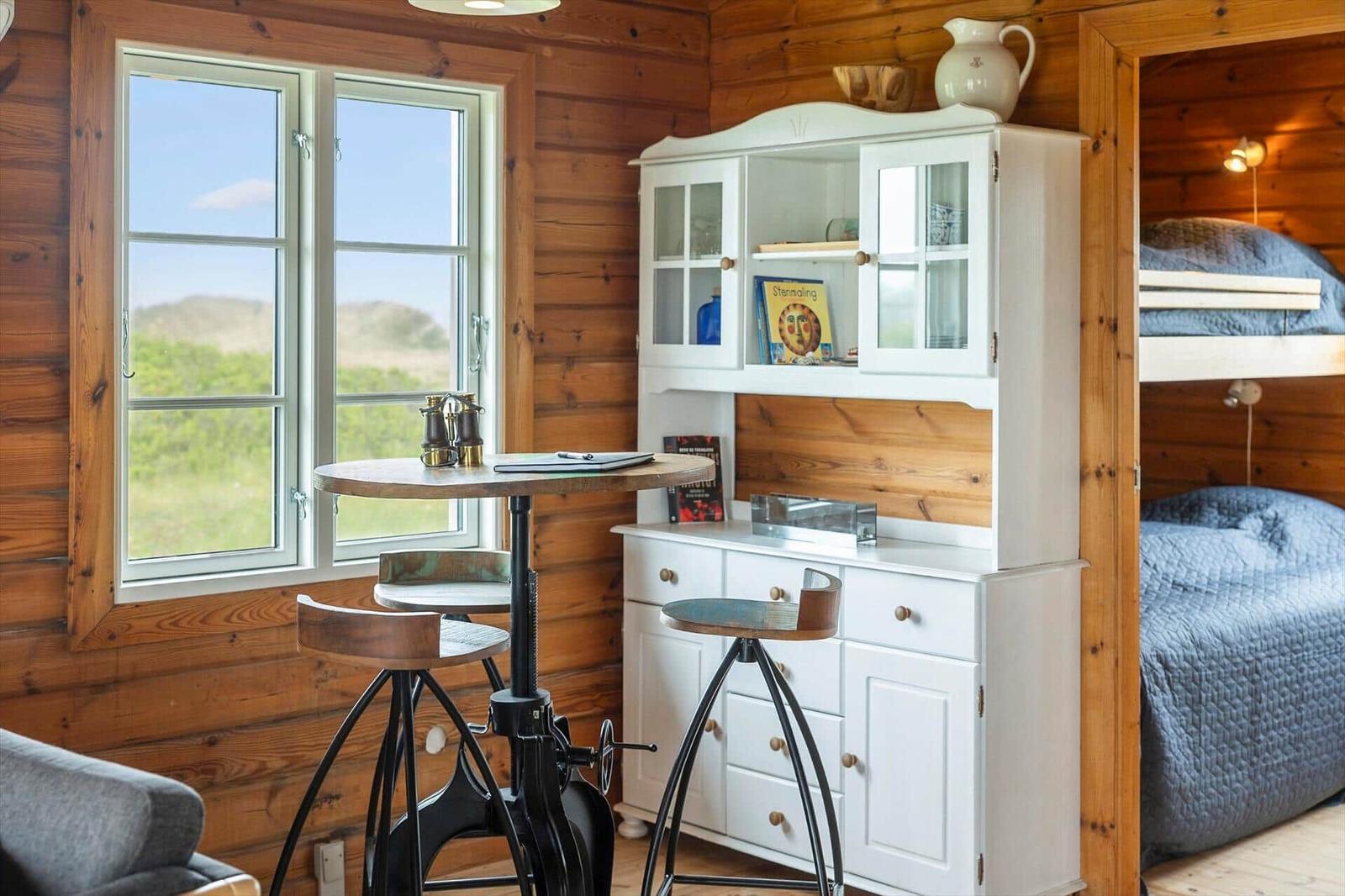 Kleiner Raum mit Holzwand, Tisch, Stühlen und Schrank. Blick auf grüne Landschaft.