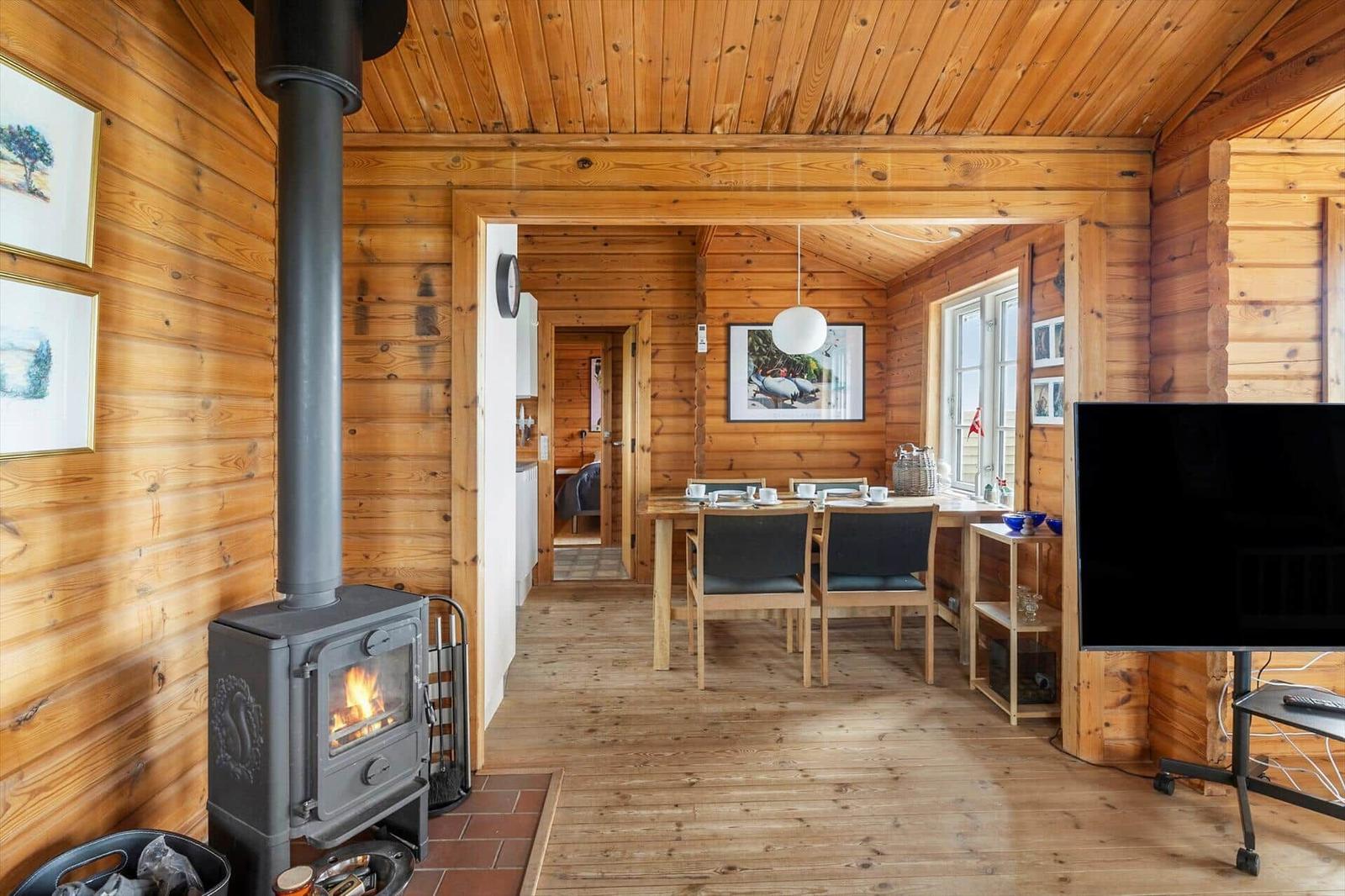 Wohnraum mit Kaminofen, Esstisch und Fernseher in Holzhaus.
