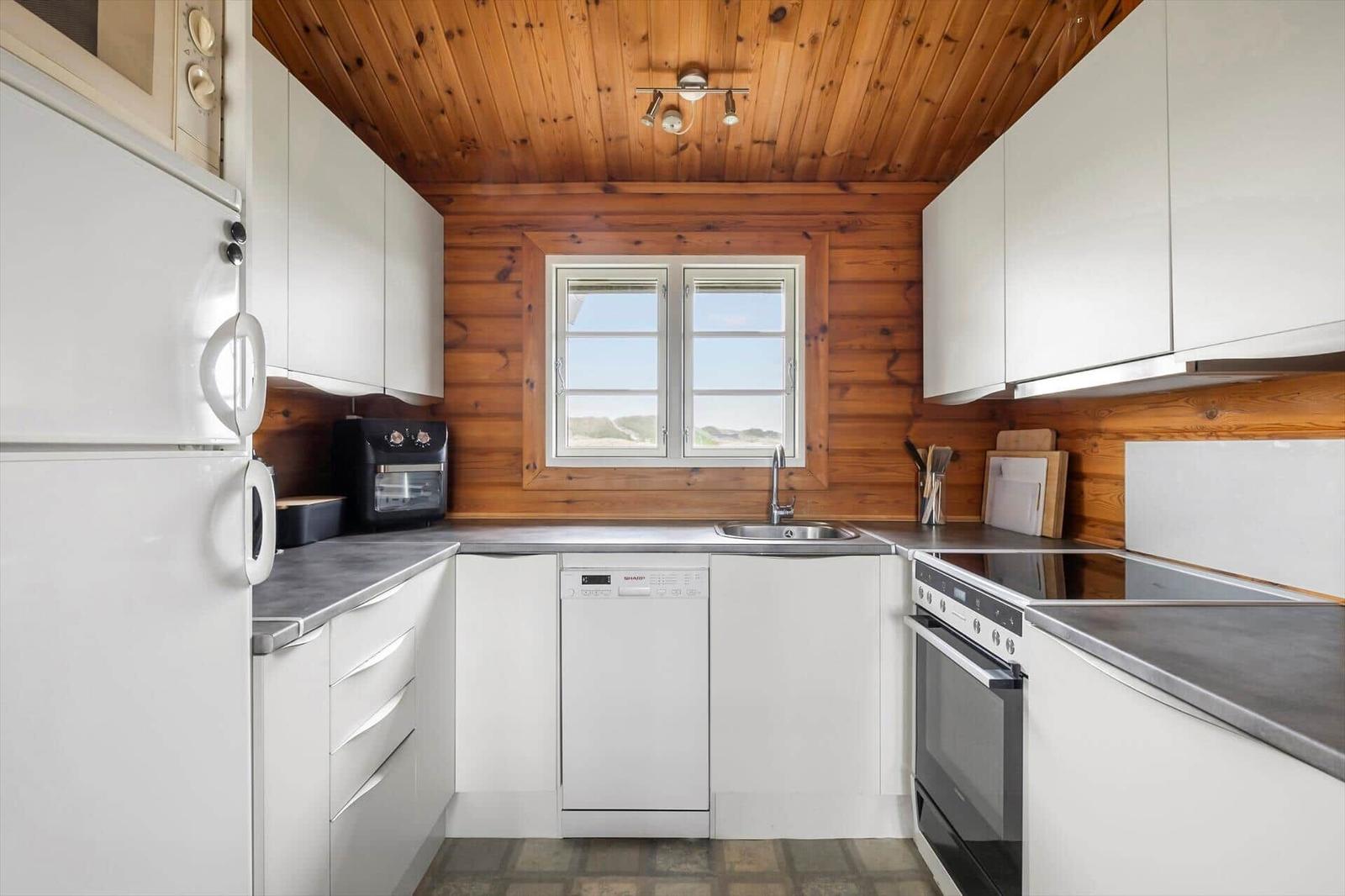 Küche mit weißen Schränken, Holzwand und -decke, Fenster, Spüle und Geräten.