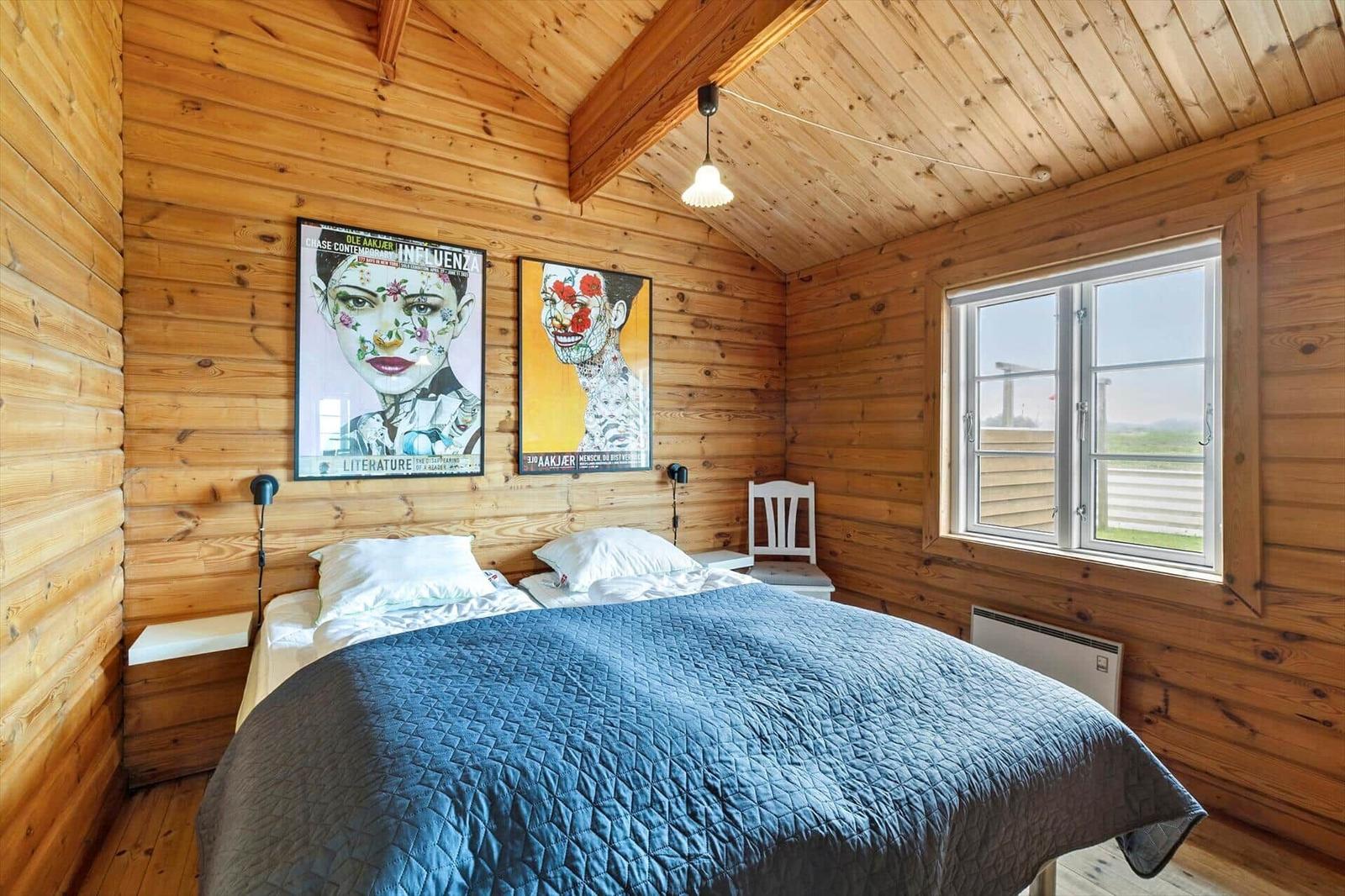 Schlafzimmer mit Holzwand, Bett, Fenster und Wandbildern.