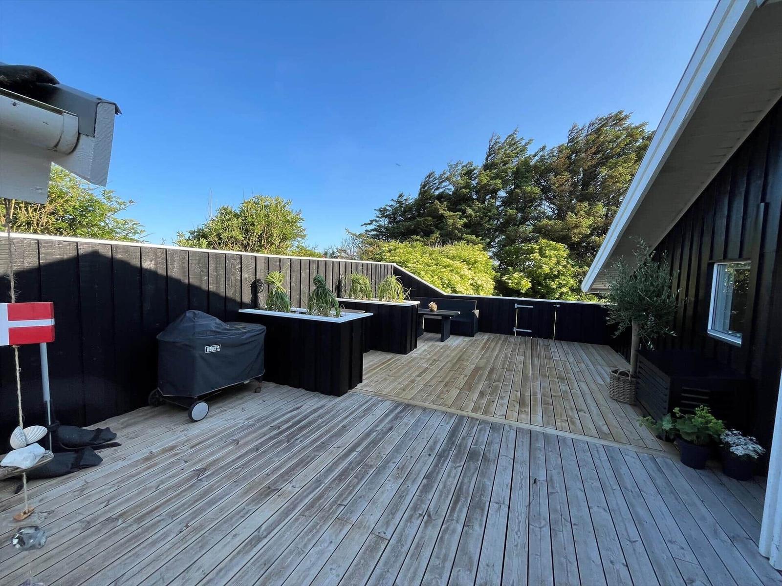 Holzterrasse mit Grill, Pflanzen und Blick auf Bäume.
