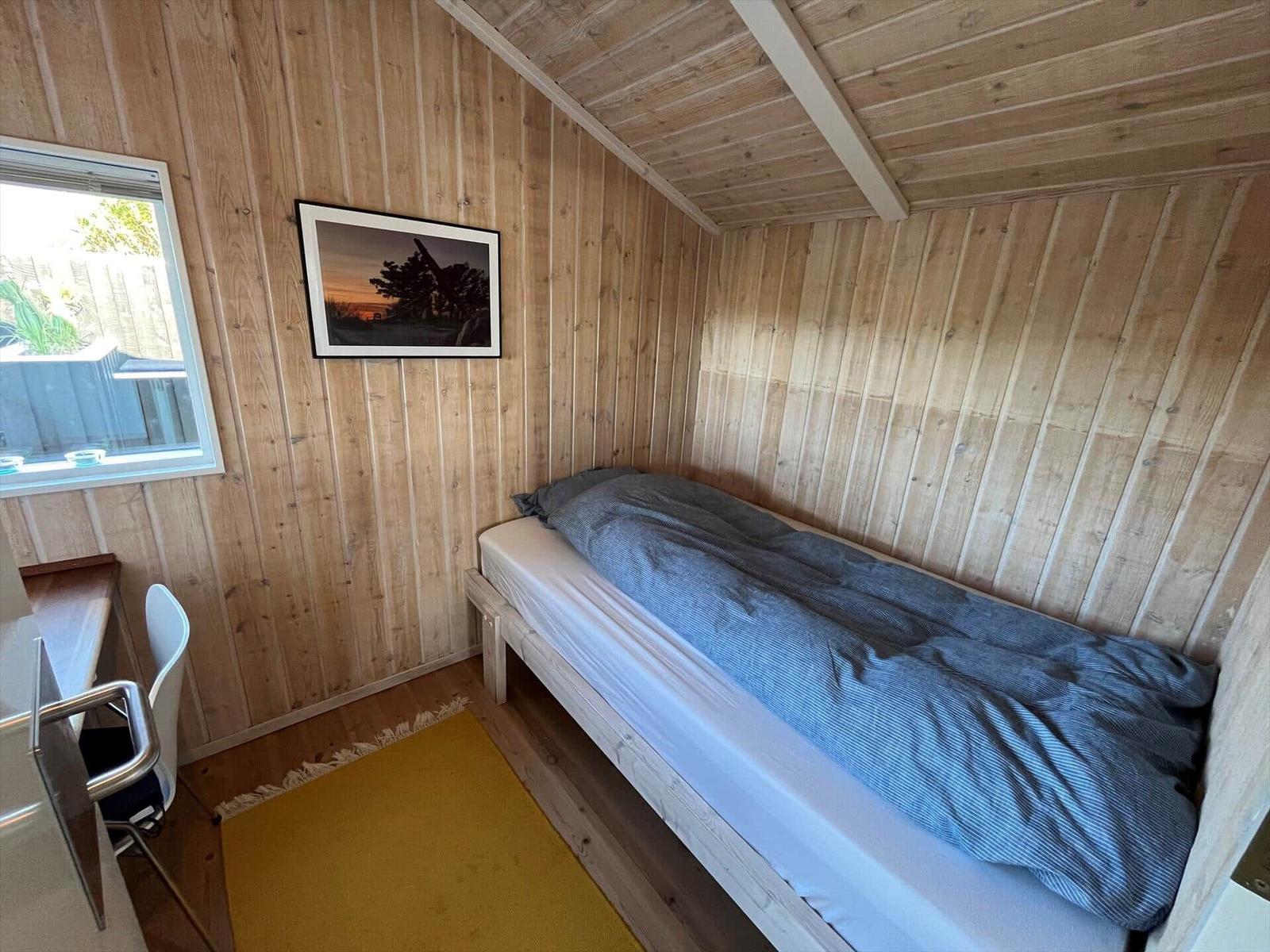 Schlafzimmer mit Bett, Fenster und Wandbild. Holzwände und Dachschräge.