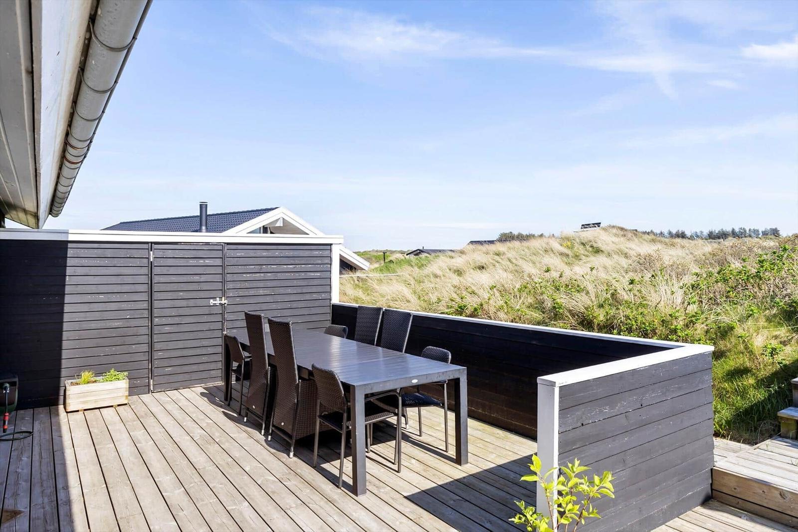 Terrasse mit Tisch und Stühlen, Blick auf Dünen und Himmel.