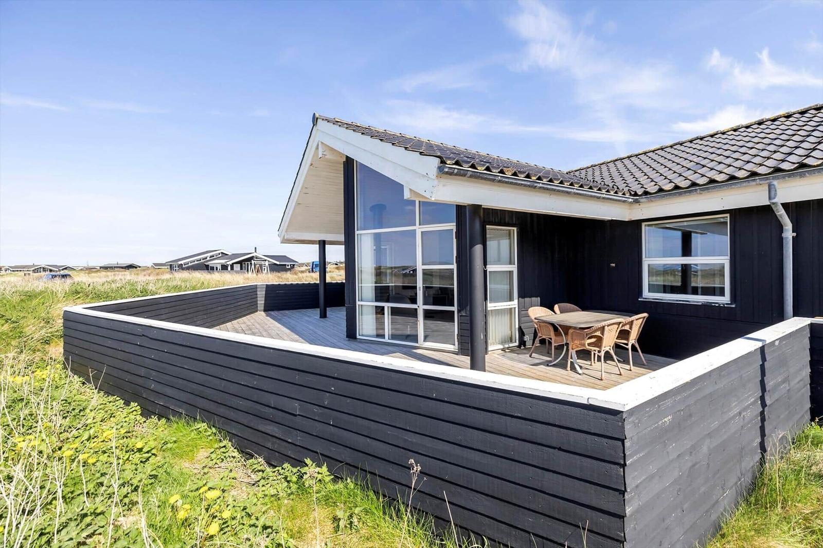 Moderne Villa mit Terrasse und Sitzgelegenheit. Schwarze Holzwandung und großes Fenster.