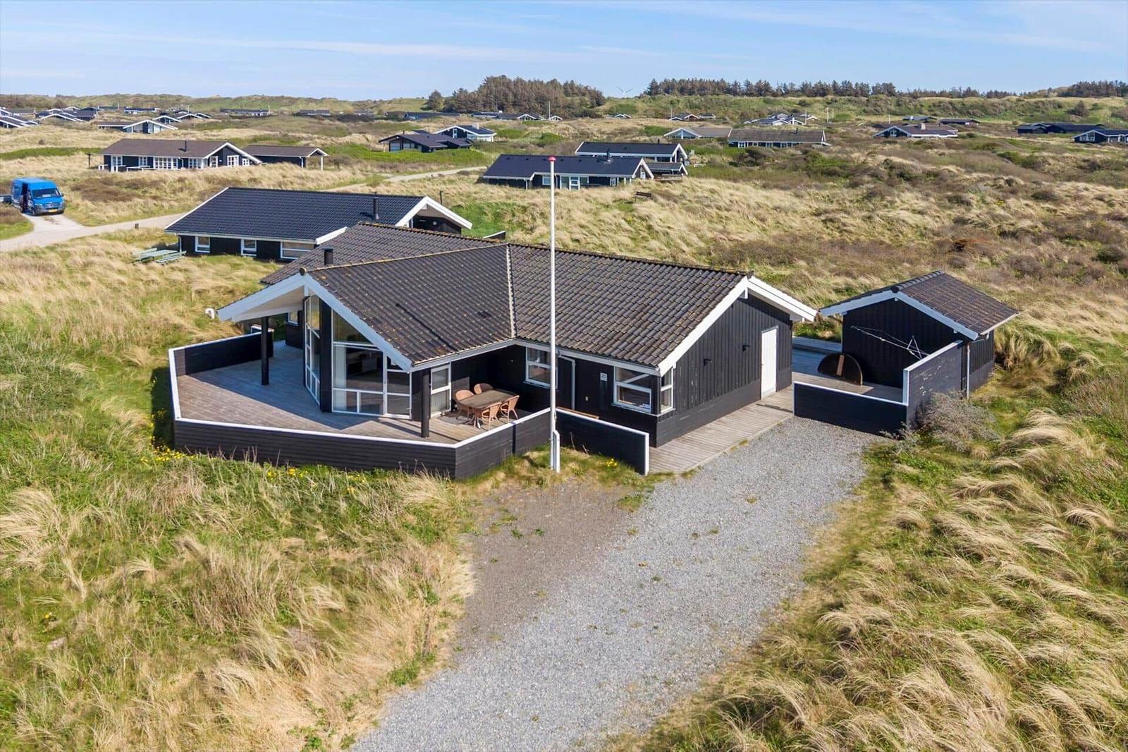 Moderne Strandhaus mit Terrasse und Grillplatz in Dünenlandschaft.