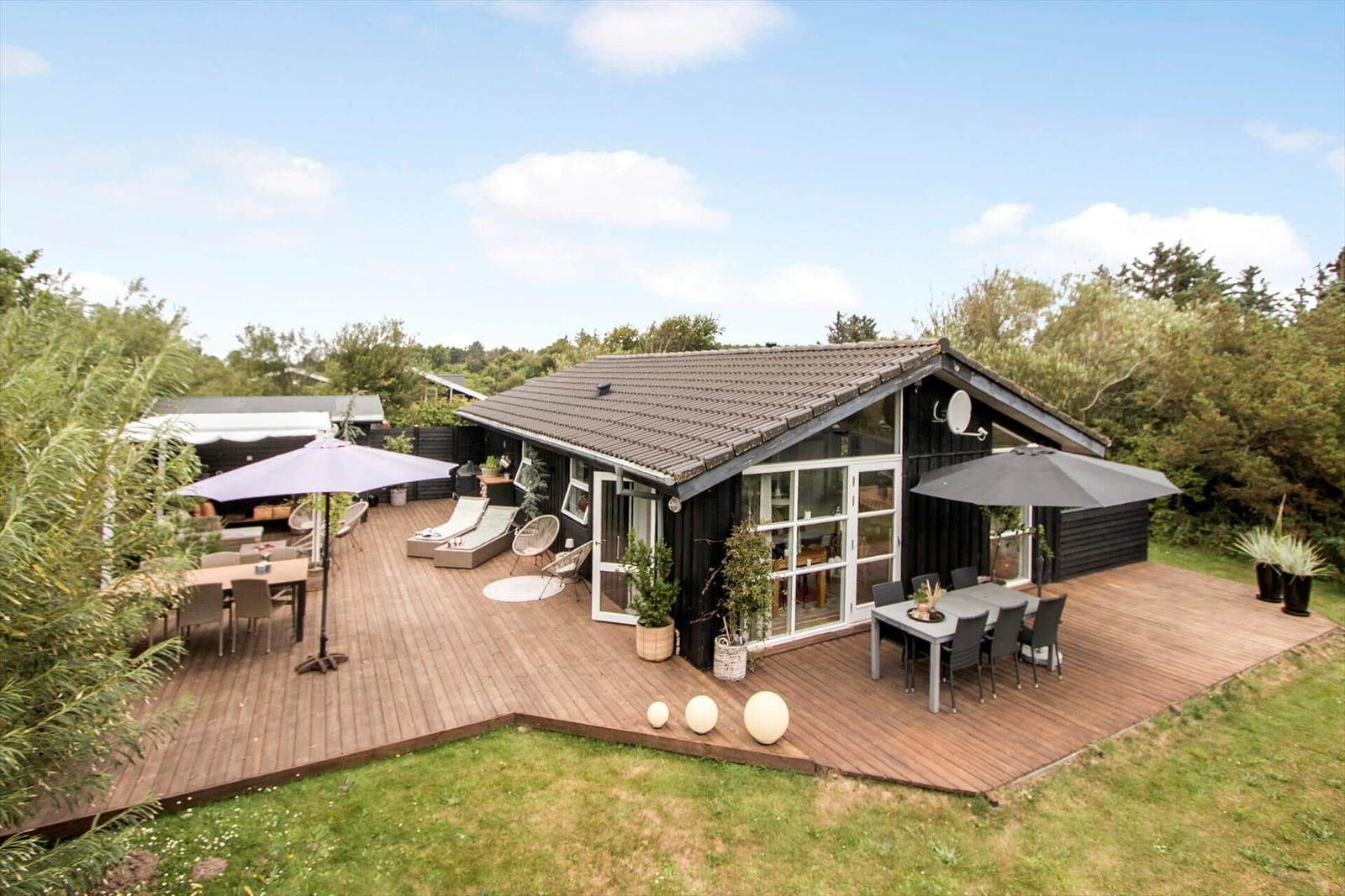 Moderne Villa mit großem Holzterrasse, Sonnenliegen und Sitzgelegenheiten im Freien.