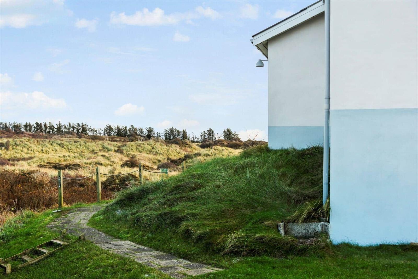 Path leads to a white wall with blue stripe. Grass and trees in background.