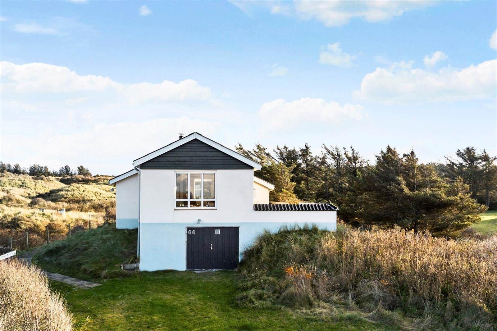 Modern villa with black roof and light blue-white facade, surrounded by grass and trees.