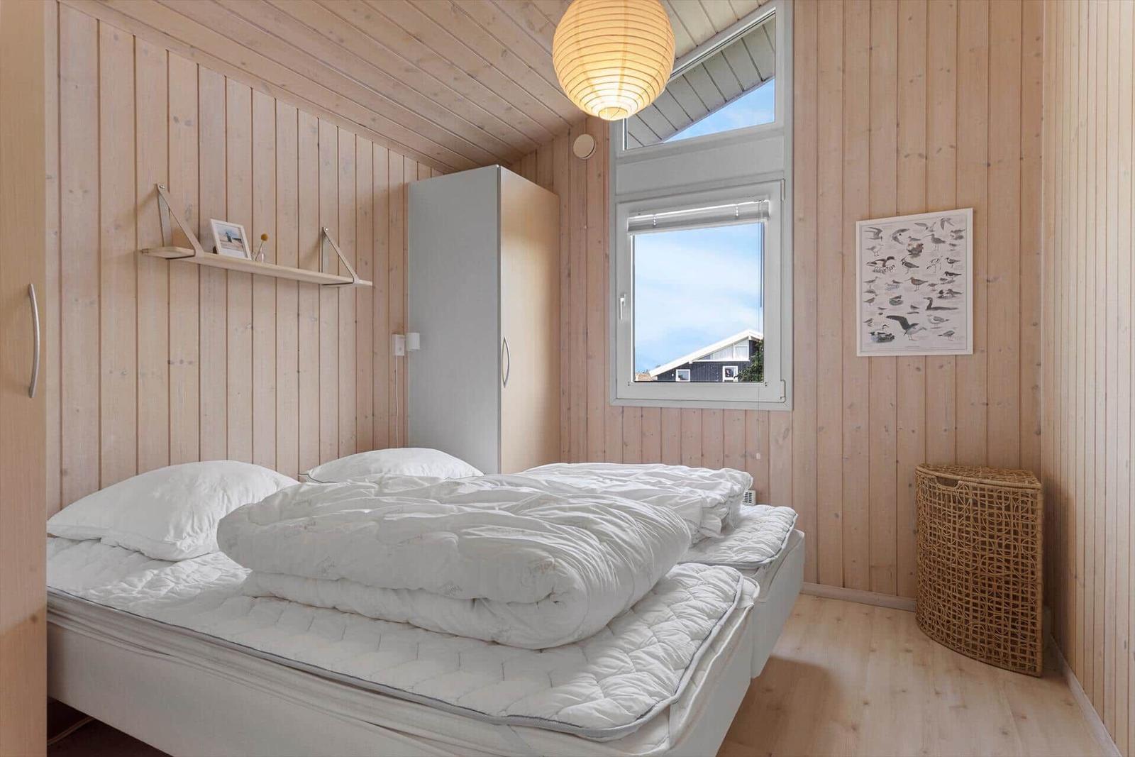 Schlafzimmer mit Holzwänden, Bett, Kleiderschrank und Fenster mit Blick.