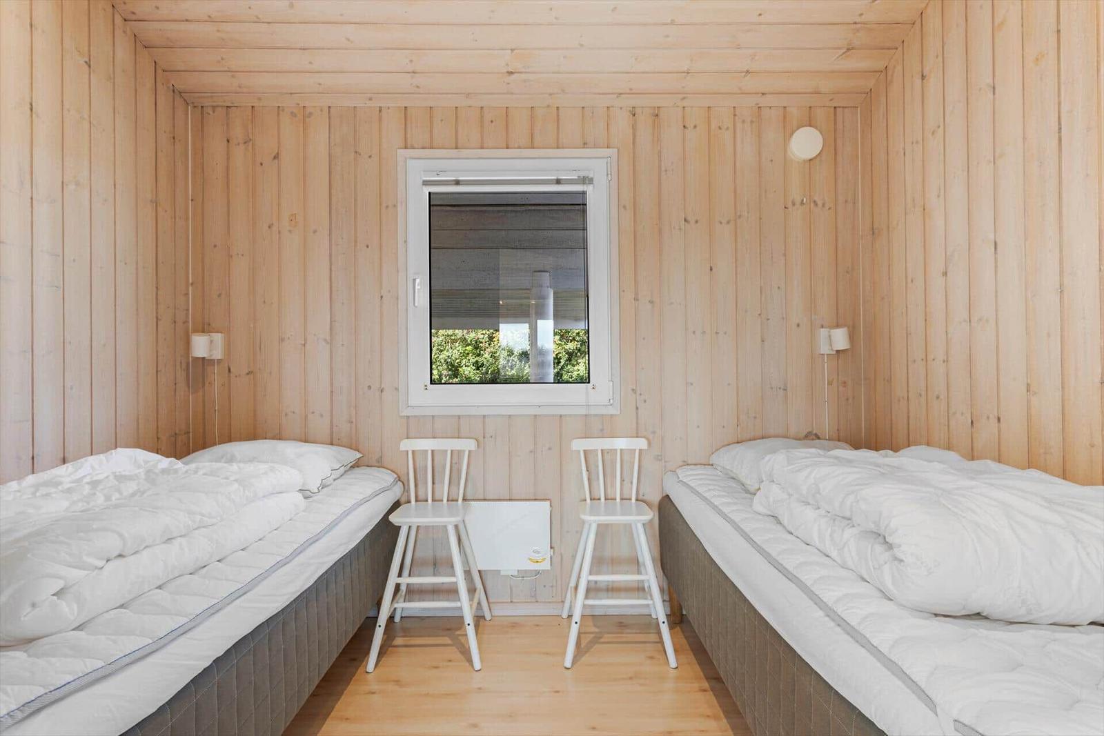 Zwei Betten mit weißen Bettwäsche, zwei weiße Stühle und ein Fenster in einem Holzraum.