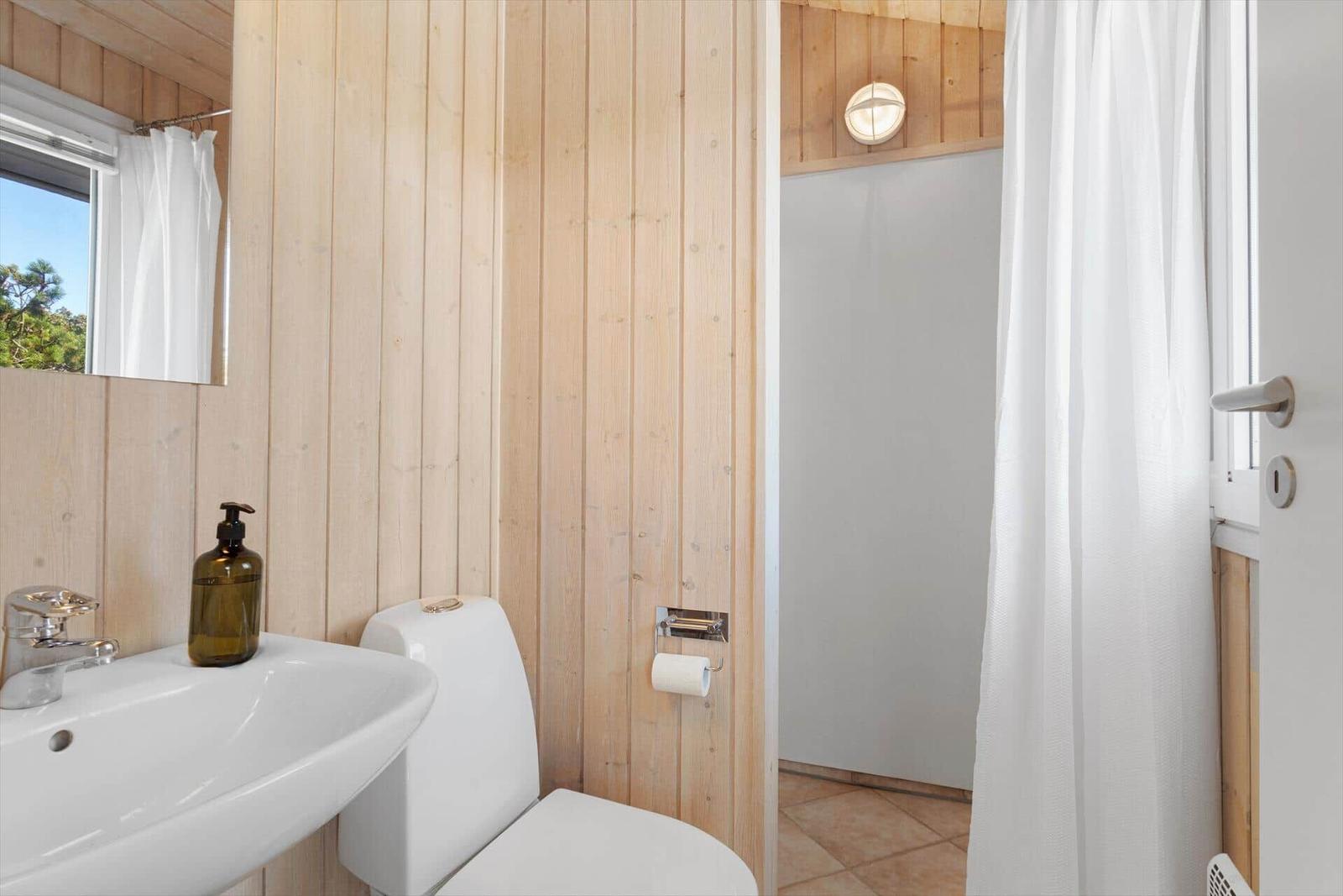 Badezimmer mit Toilette, Waschbecken und Dusche mit weißen Vorhängen.