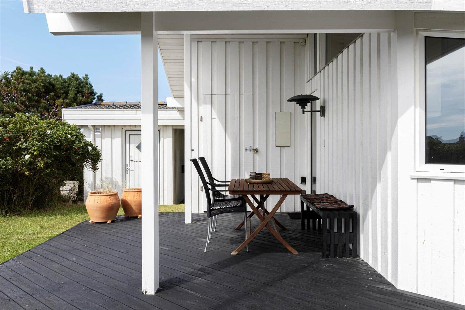 Terrasse mit Tisch, Stühlen und Bank vor weißer Hauswand.