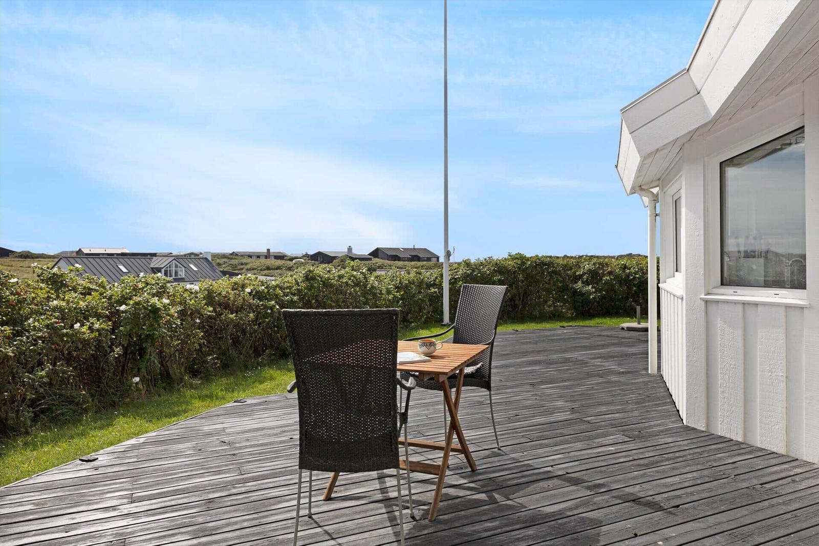 Terrasse mit Tisch und zwei Stühlen. Blick auf Grünflächen und Häuser im Hintergrund.