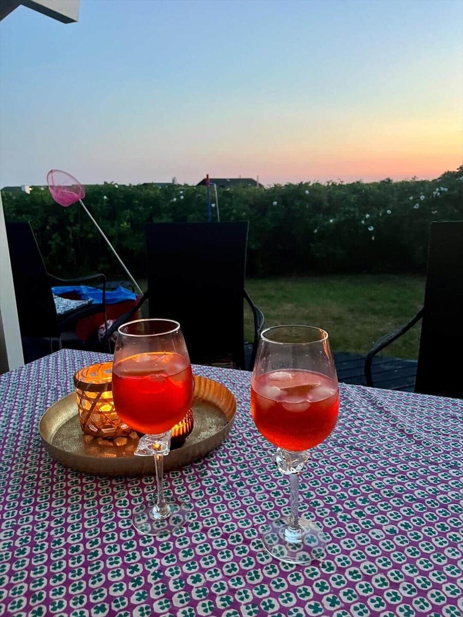Zwei Gläser mit Getränk stehen auf einem Tisch mit Tischdecke. Im Hintergrund ist ein Garten und Sonnenuntergang.