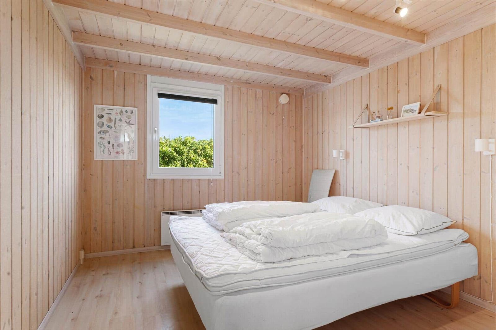 Schlafzimmer mit Holzwand, Bett und Fenster mit Blick auf Grün.