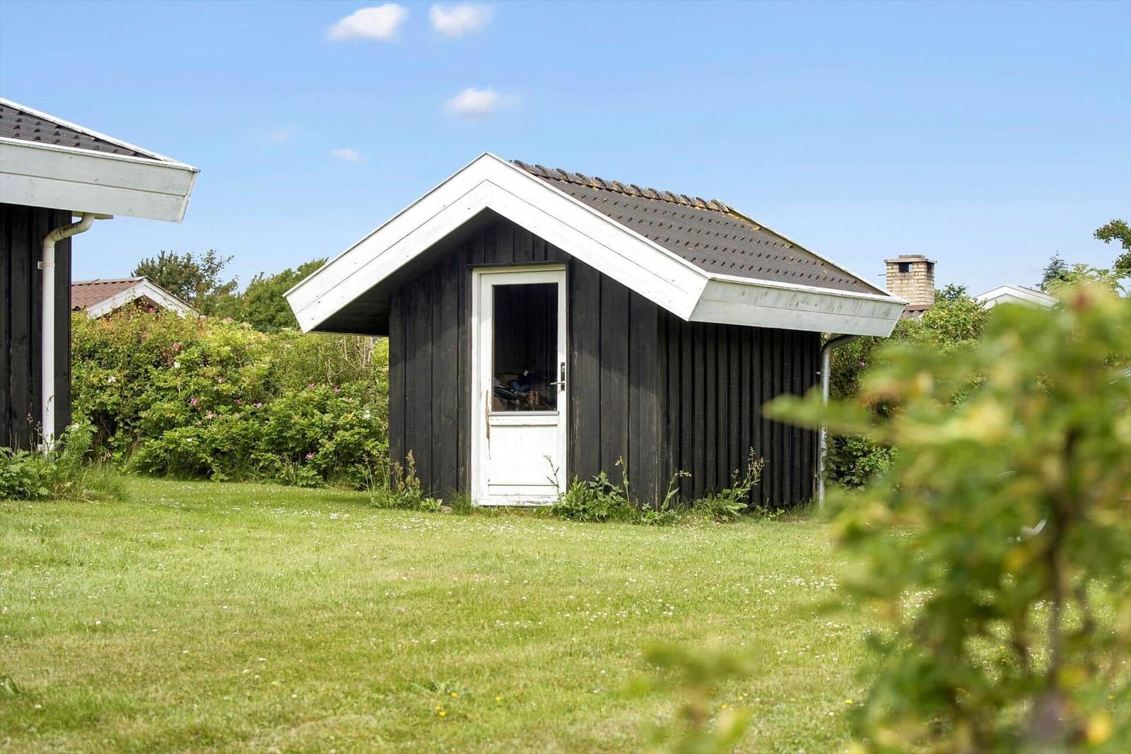 Holzschuppen mit weißer Tür und Dachkante im Garten
