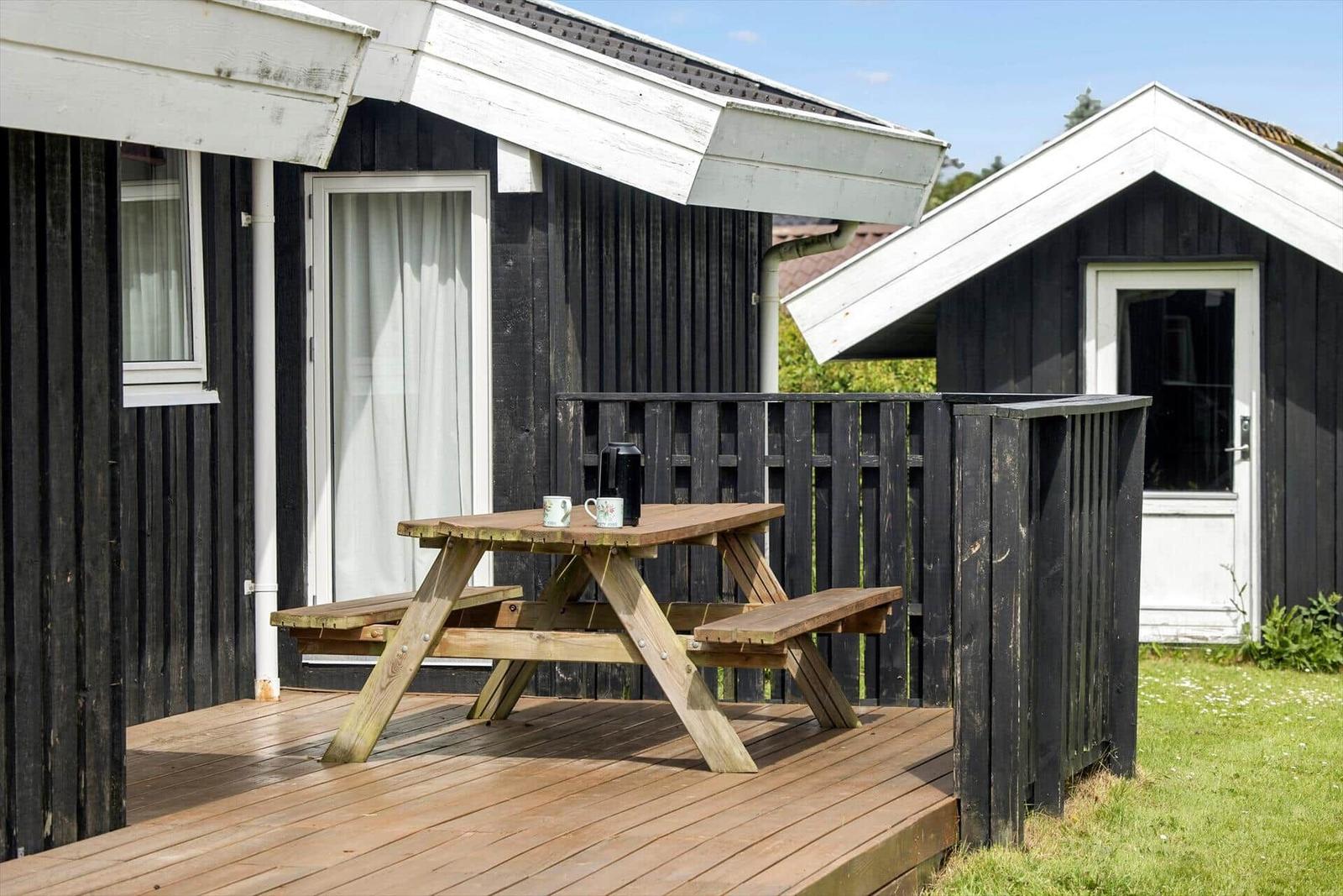 Holztisch mit zwei Stühlen auf einer Terrasse vor einem Haus mit schwarzer Fassade.