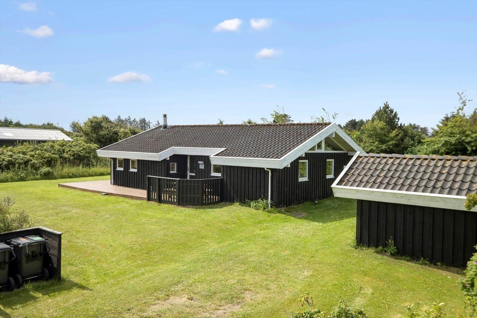 Schwarzes Holzhaus mit Terrasse und Garten. Umgeben von Bäumen und Gras.
