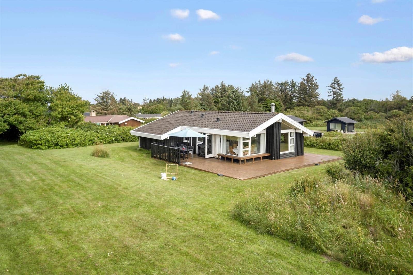 Moderne Villa mit Terrasse und Garten. Blick auf umliegende Bäume und klaren Himmel.