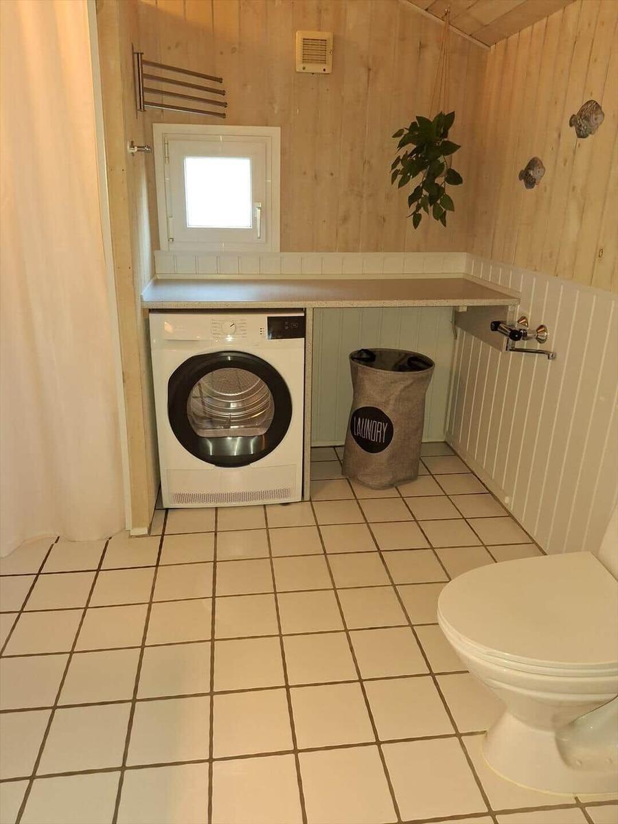 Waschmaschine und Toilette in einem Raum mit Holzwänden und Fliesenboden.