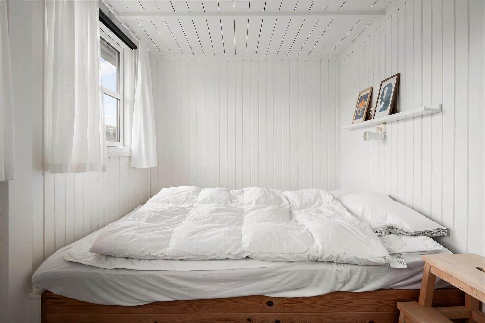 Ein Schlafzimmer mit weißer Wandverkleidung, einem Bett und einem Fenster.