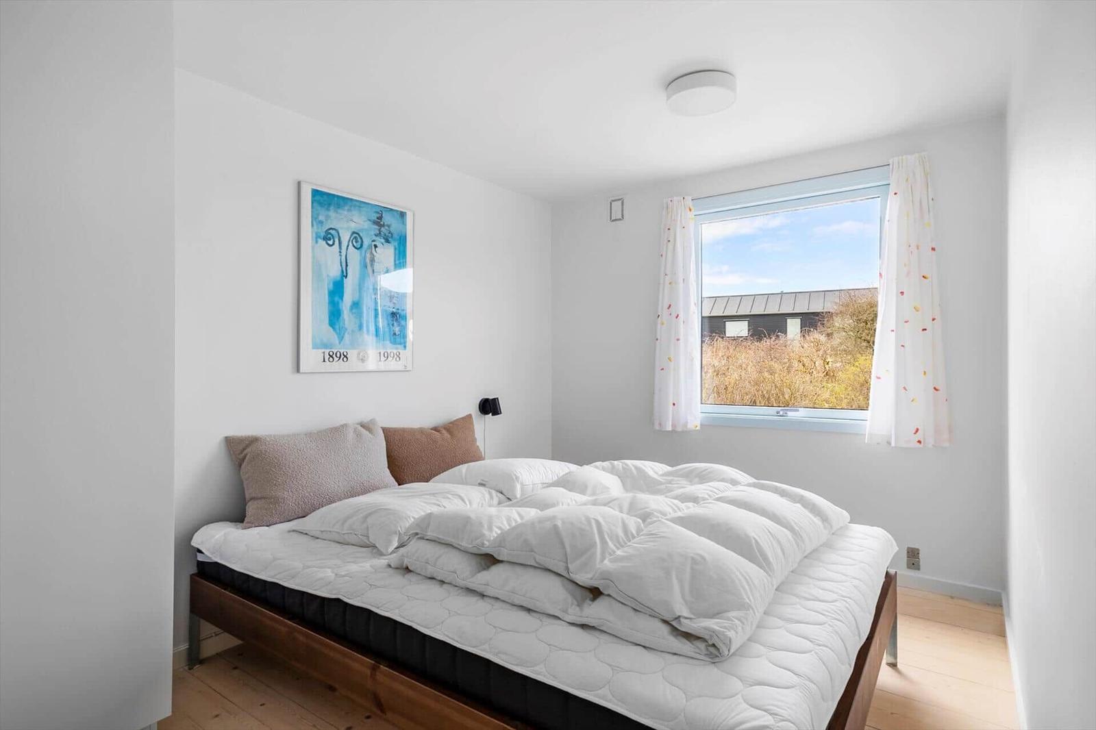 Schlafzimmer mit Bett, Fenster und Wandbild.