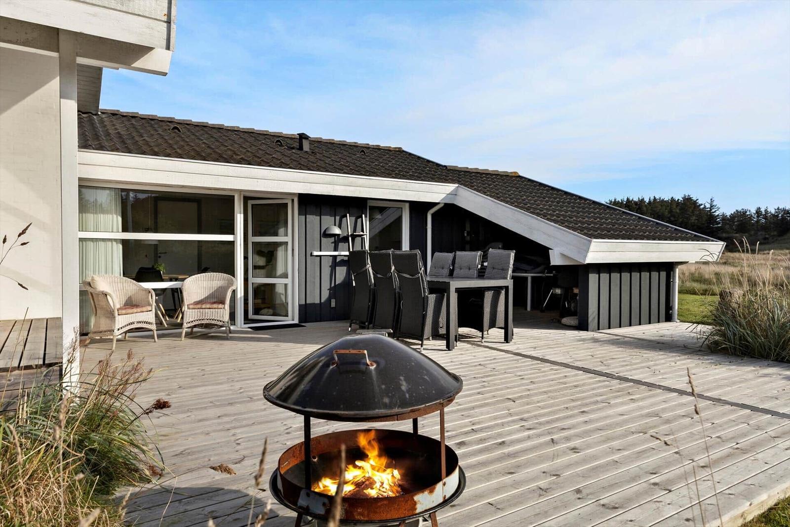 Terrasse mit Grill und Sitzgelegenheiten vor einem Haus mit großem Fenster.