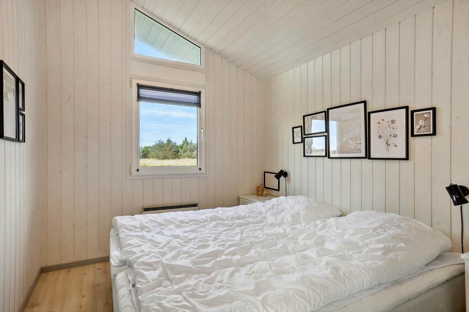 Schlafzimmer mit weißer Bettwäsche, Holzwänden und Fensterblick auf Grünfläche.