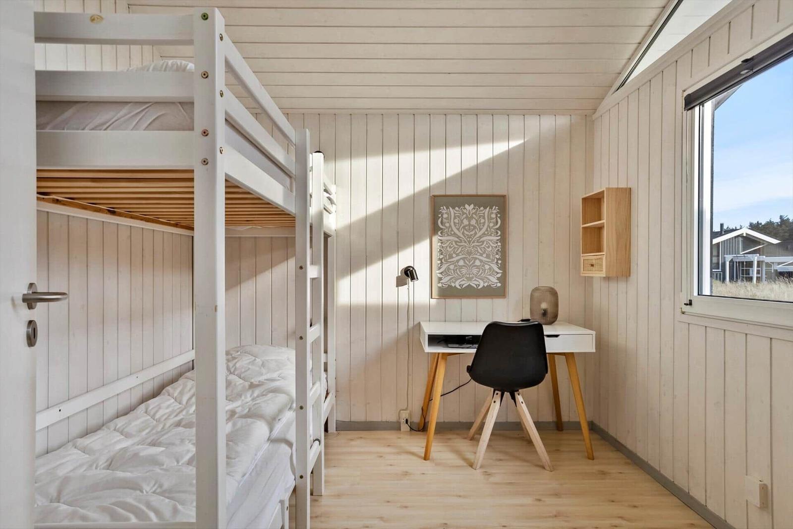 Zimmer mit Doppelstockbett, Schreibtisch und Fenster.