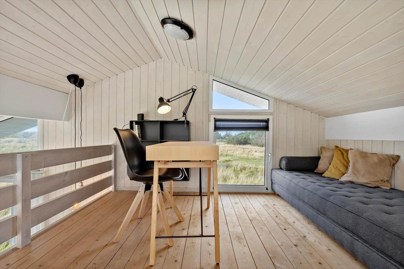 Ein Raum mit Schreibtisch, Sofa und großem Fenster mit Blick auf die Landschaft.