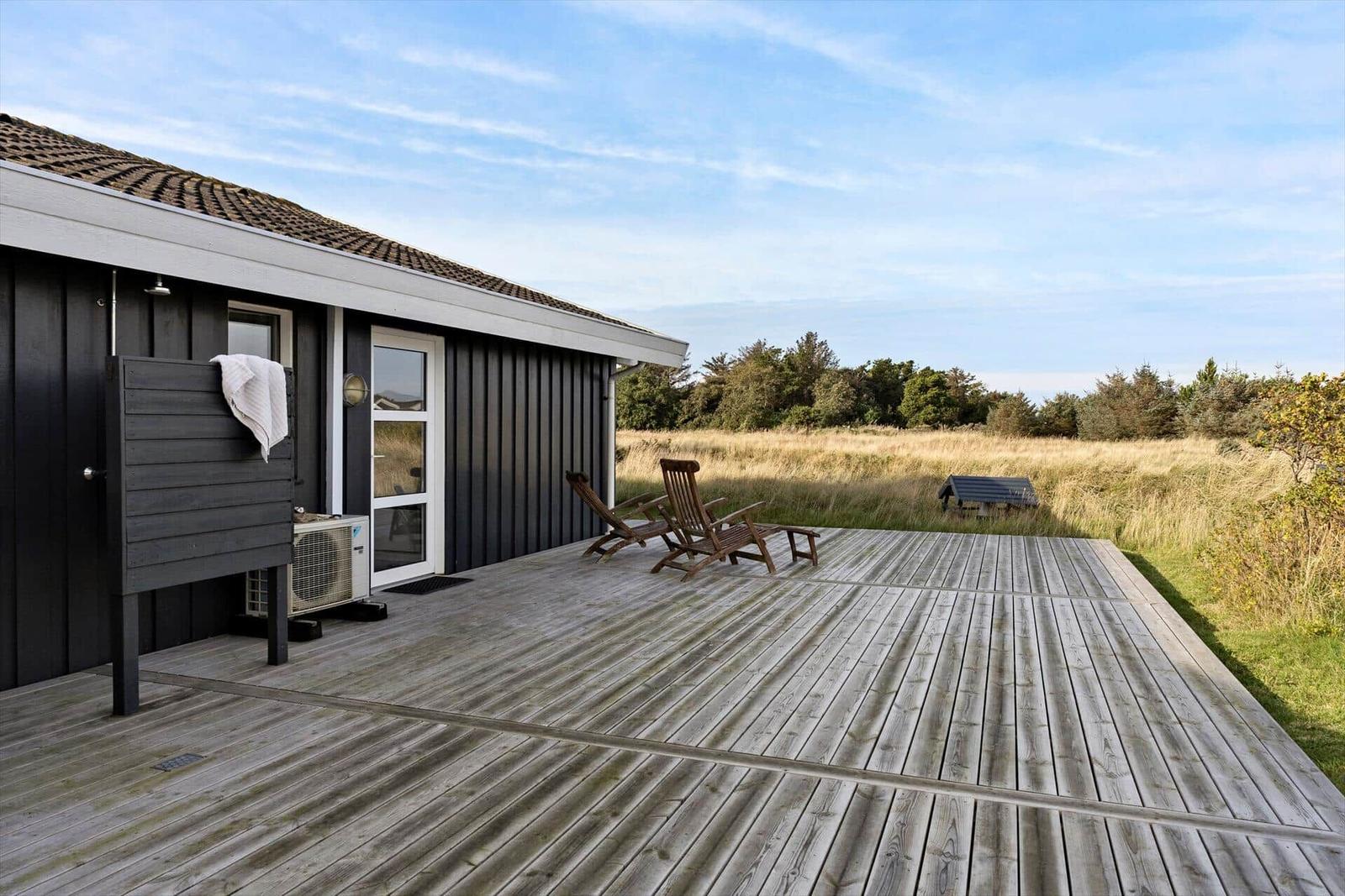 Holzterrasse mit Liegestühlen vor einem Haus mit dunklem Holzschindeldach.