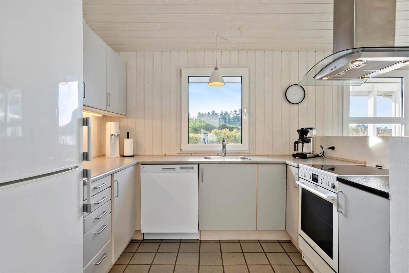 Küche mit weißen Schränken, Spüle, Herd und Fenster mit Blick auf Grün.