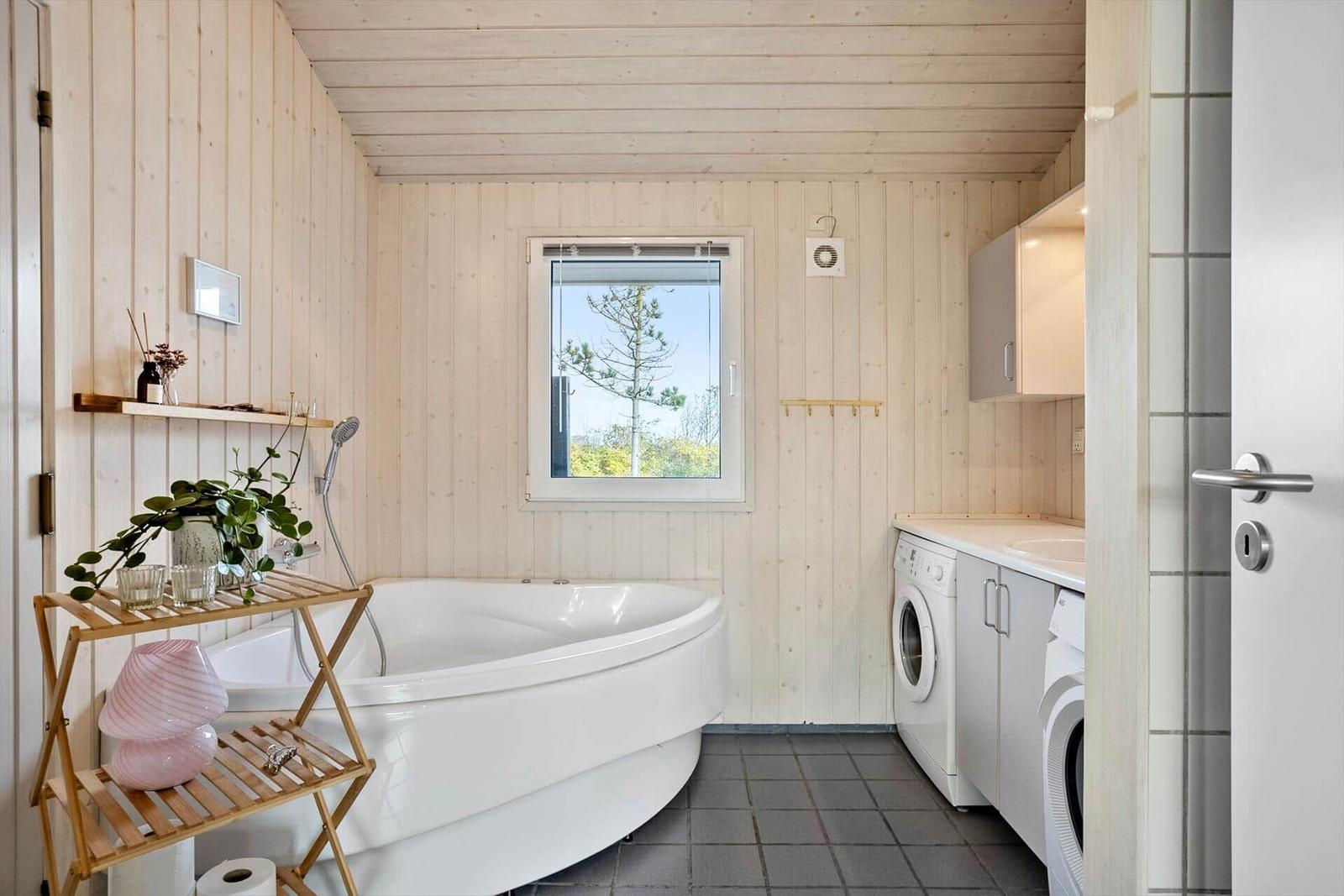 Badezimmer mit Badewanne, Waschmaschine und Fenster mit Blick auf Baum.