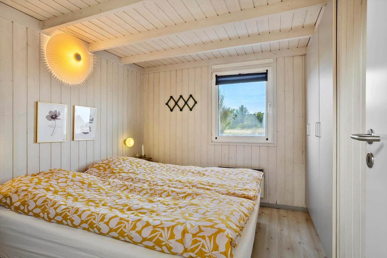 Schlafzimmer mit Bett, Fenster und Holzwandverkleidung.