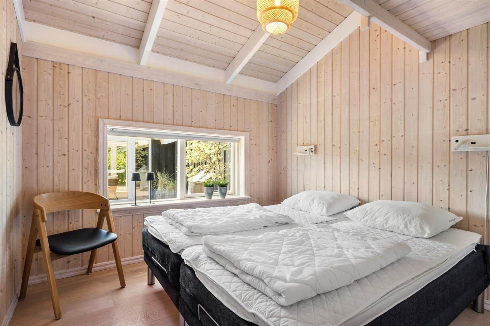 Schlafzimmer mit Holzwand, Bett und Fenster zum Garten.