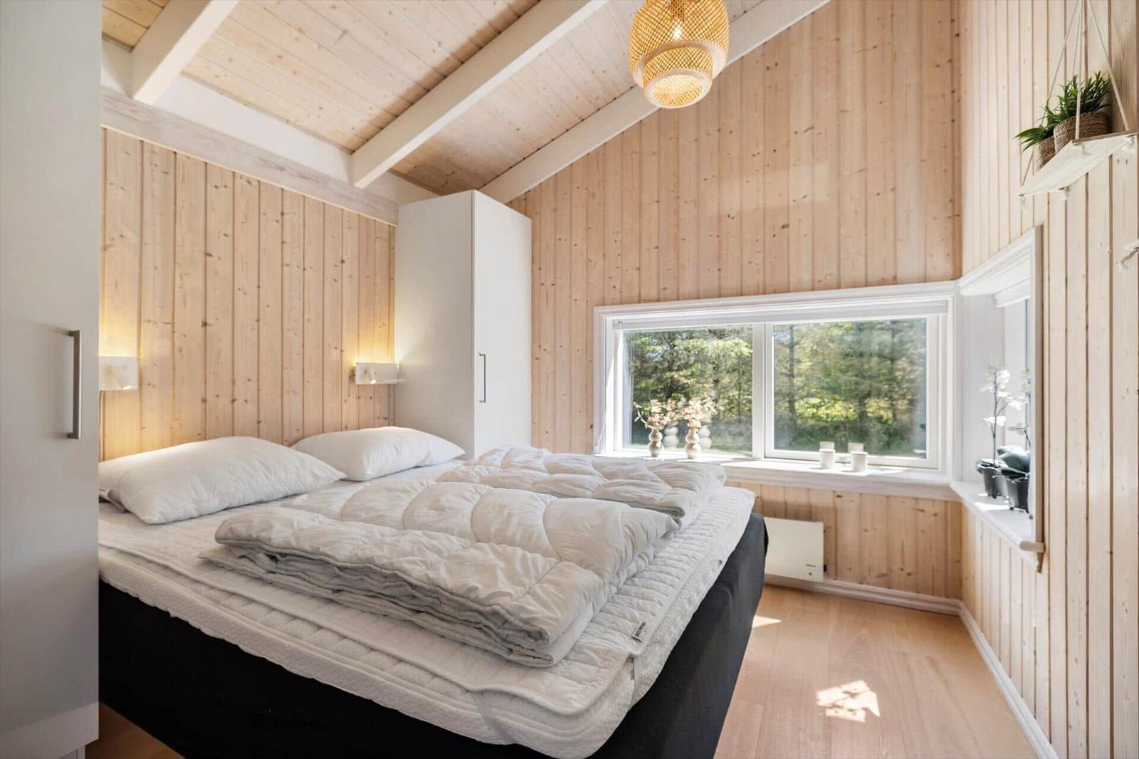 Schlafzimmer mit Holzwand, Bett und Fenster mit Blick auf Bäume.