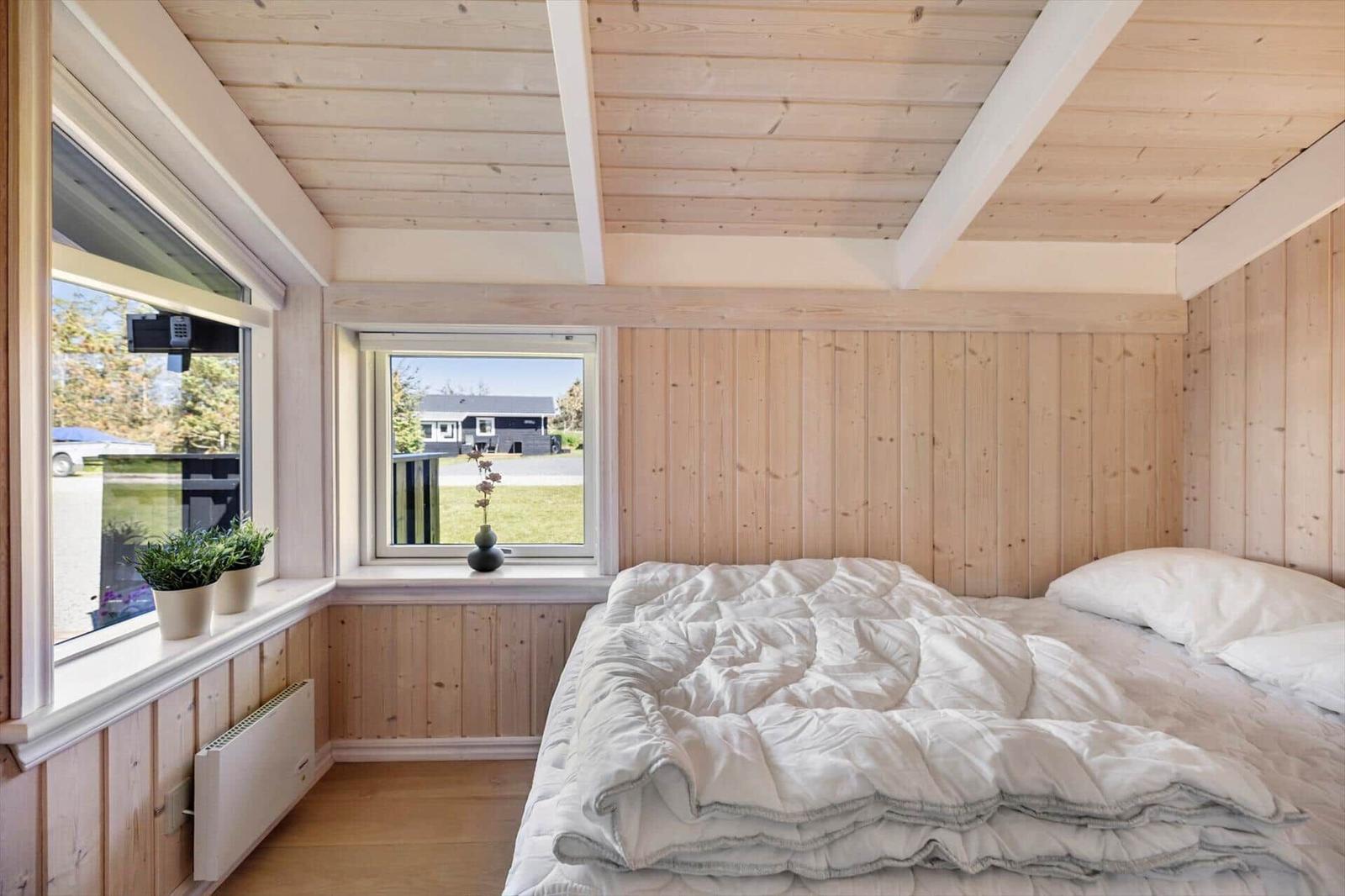 Schlafzimmer mit Holzwänden, Bett und Fenstern mit Blick nach draußen.