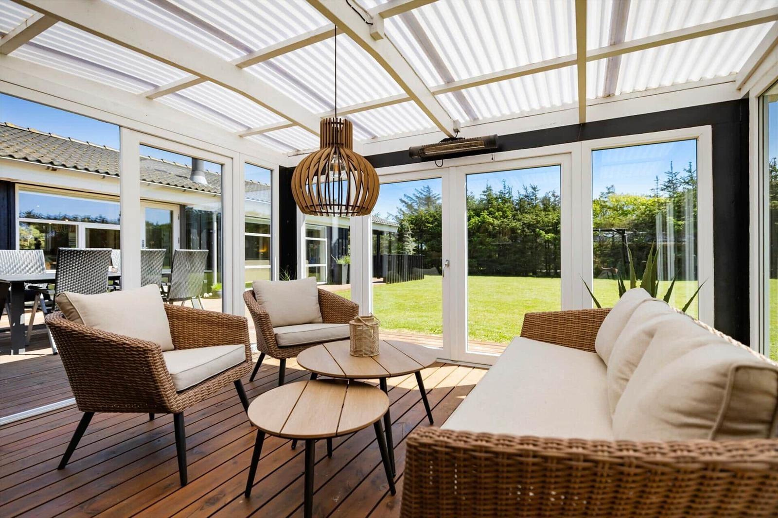 Terrasse mit Sitzgruppe, Tischen und Decke. Blick auf Garten und Haus.