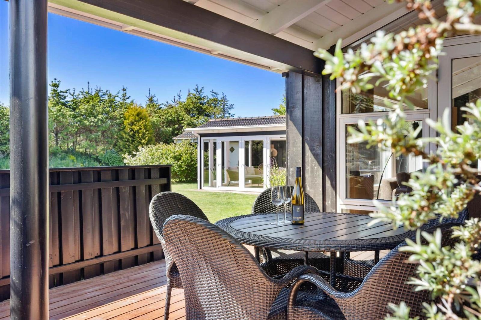 Terrasse mit Tisch und Stühlen, Blick auf grünen Garten und Haus.