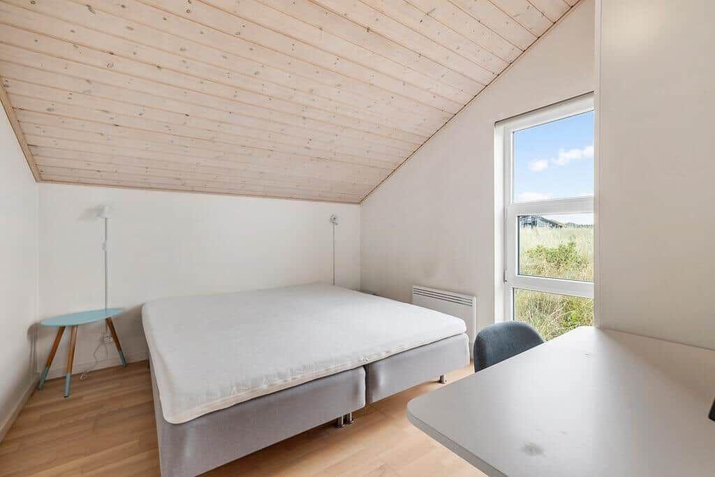 Schlafzimmer mit Bett, Schreibtisch und Fenster mit Blick auf Gras.