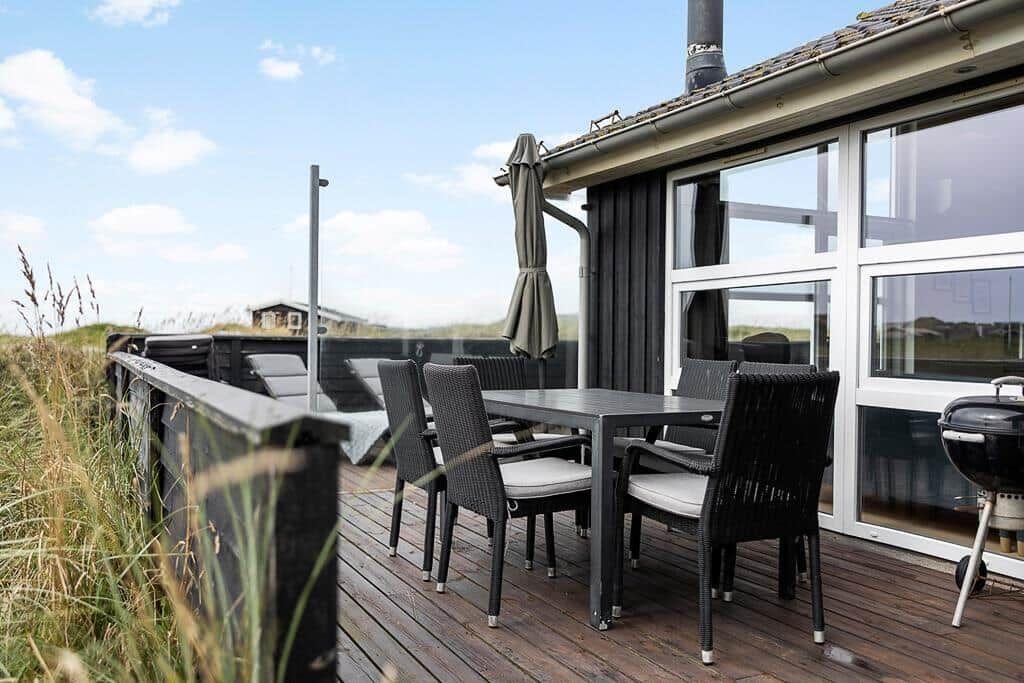 Terrasse mit Tisch, Stühlen und Grill. Hintergrund: Gras und Gebäude.